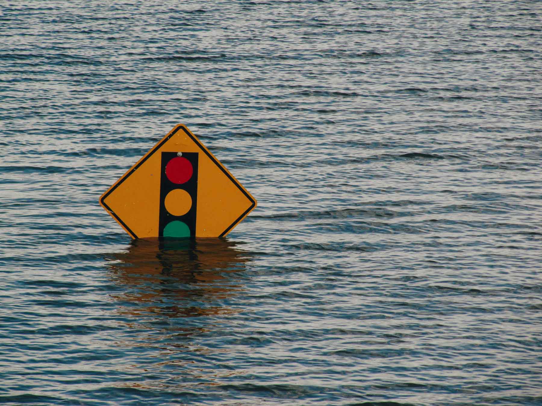A flooded street traffic sign, its base submerged in rising water