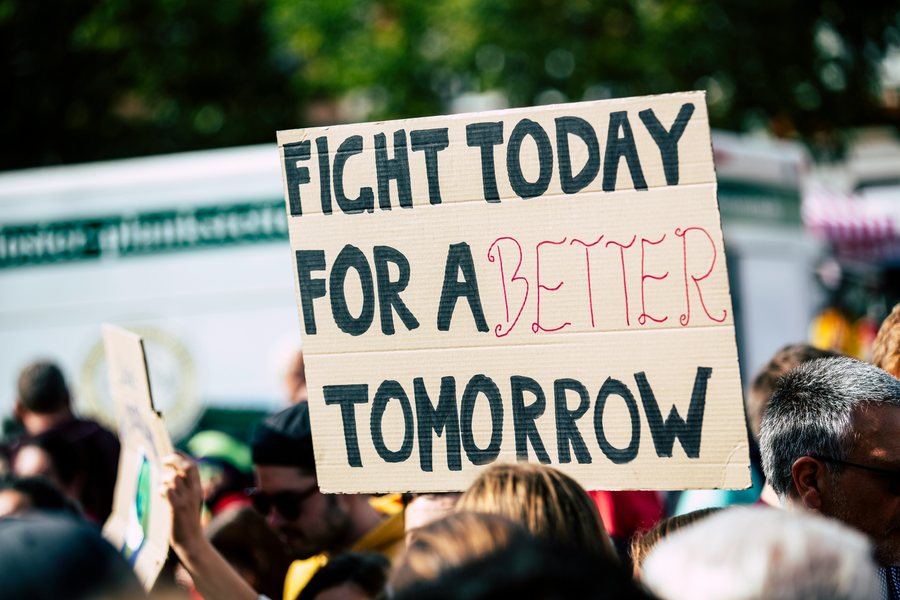A climate protester holding a hand-drawn sign reading "Fight today for a better tomorrow"