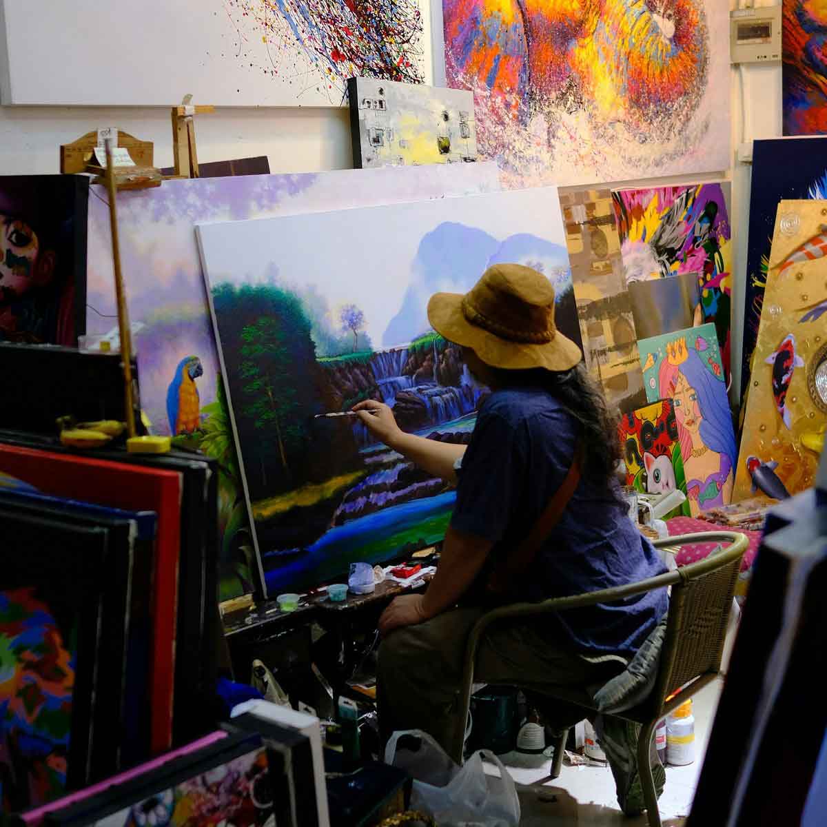 An artist painting a landscape in a studio surrounded by colourful artwork